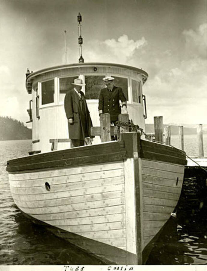 Two men stand on a boat at the Government dock in Coolin, Idaho. Taken during the winter. Donated by Russ Bishop through Priest Lake Museum.
