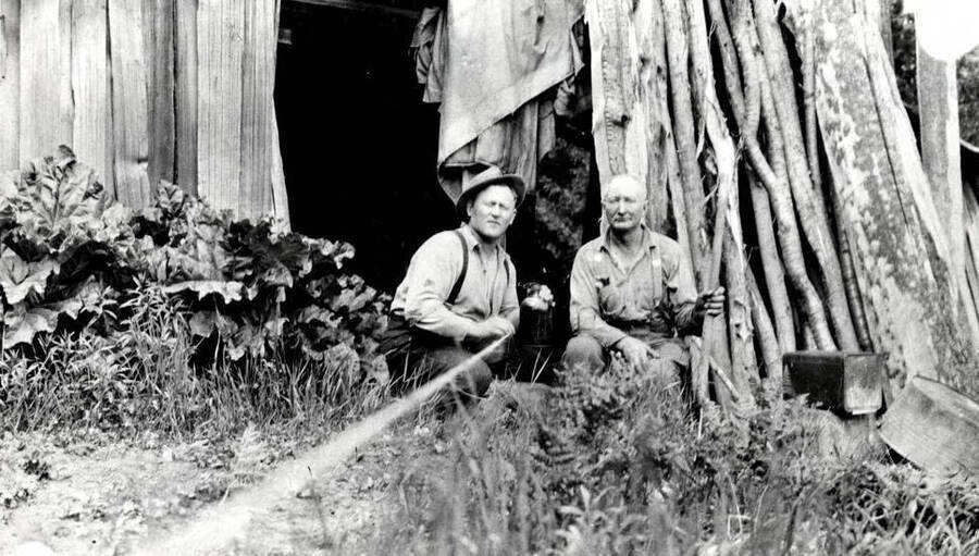 Lewis 'Pete' Chase sits next to an unidentified photographer. The photographer has a string pulley attached to the camera in order to take the picture.