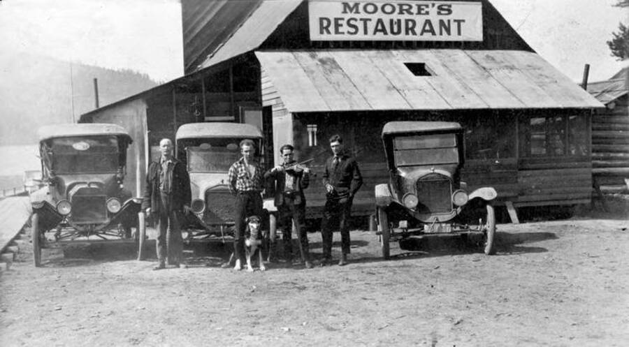Four men and one dog stnading outside of Moore's Restaurant. One man is holding a violin. Donated by U of I Library through Priest Lake Museum.