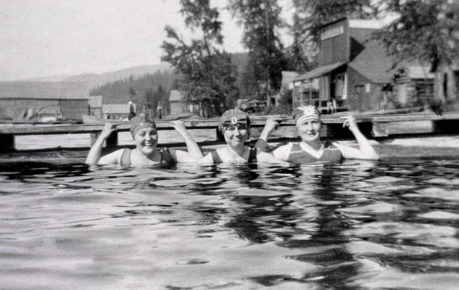 Edith Phelan, Harriet Kline, and Mrs. Fussy holding onto a dock while swimming. Coolin, Idaho. Donated by Harriet (Klein) Allen through Priest Lake Museum.