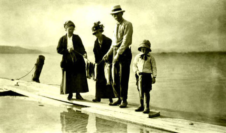 Two women, one man, and one child stand on a dock holding the fish they caught. Donated by Viv Beardmore through Priest Lake Museum.