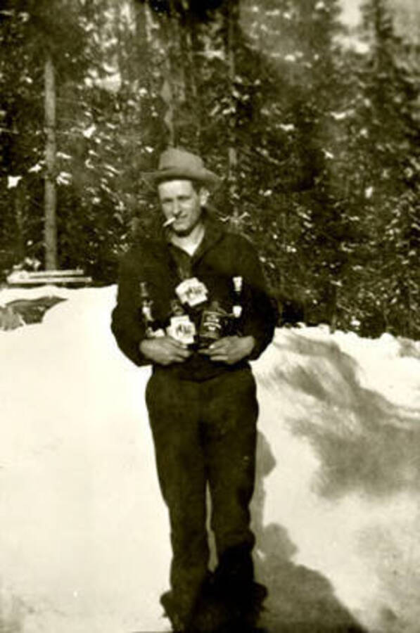 Ralph Miller stands holding whiskey bottles. Donated by Red Gasterneau through Priest Lake Museum.