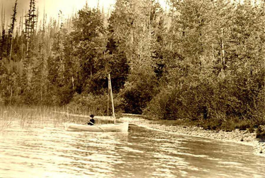 View of a woman sitting alone in a sailboat. Priest Lake, Idaho. Donated by Harriet (Klein) Allen via Priest Lake Museum.