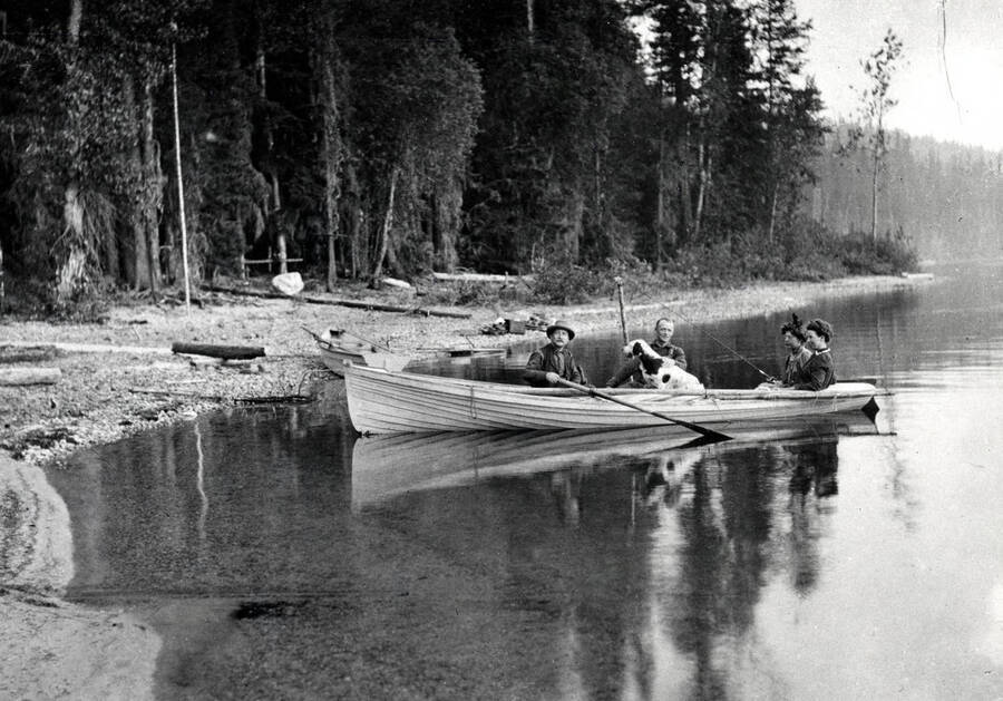 Two men, two women, and a dog in a rowboat docking on the beach.
