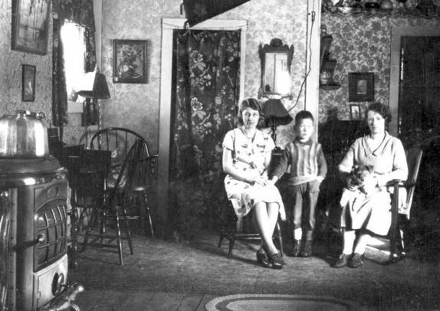 Inside of Huot's camp home. Two women, one boy, and a dog sit for a photograph. Donated by Dewey Huot through Priest Lake Museum.