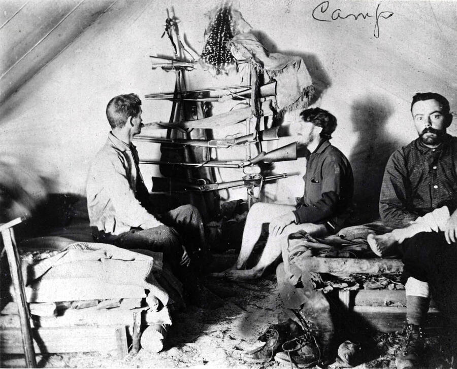 Three men inside a tent. A gun rack can be seen in the background. Donated by Harriet (Klein) Allen through Priest Lake Museum.