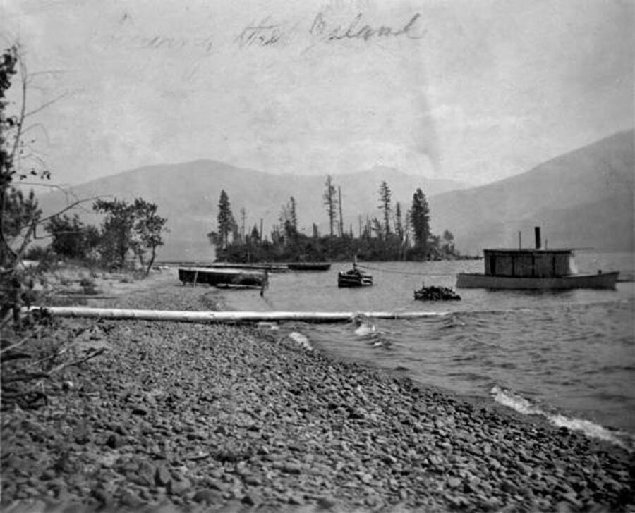 View of a boat tied to pilings. An island can be seen in the background. Donated by Stan McClung through Priest Lake Museum.
