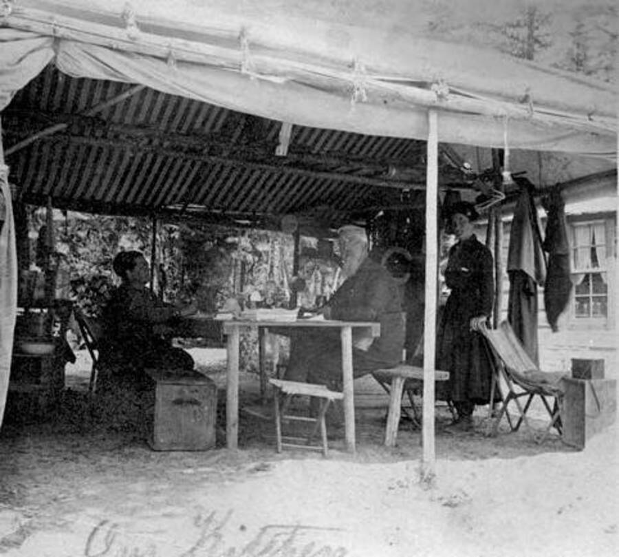 People sitting and standing in an outdoor kitchen. Donated by Stan McClung through Priest Lake Museum.