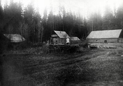 A small girl can be seen standing on a stack of lumber at unidentified logging camp.