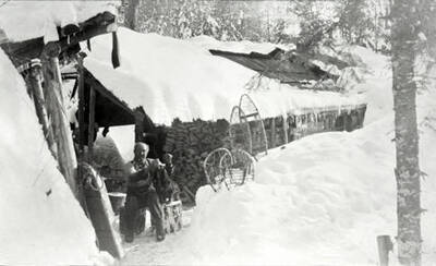 Pete Chase sitting outside a cabin with a dog. Donated by Marjorie Paul Roberts via Priest Lake Museum.