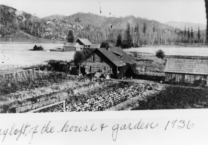 A rustic house surrounded by a cultivated garden, with another building nearby. Behind the structures are open fields and a line of trees. Hills rise in the background, framing the scene. Handwritten text at the bottom reads: "of the house & garden 1936".