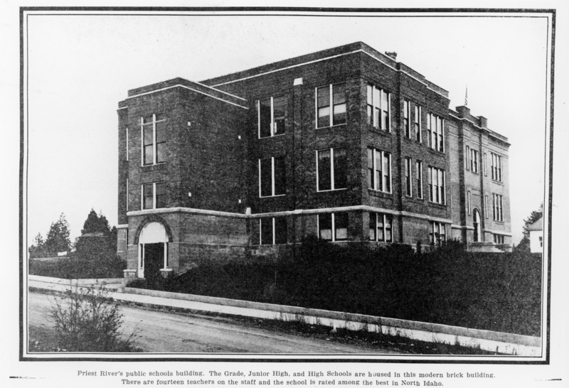 A large, three-story brick building with several windows. There is an archway at the entrance, and the structure is surrounded by bushes and a sidewalk. Trees are visible in the background. Label near bottom reads: "Priest River public schools building. The Grade, Junior High, and High Schools are housed in this modern brick building. There are fourteen teachers on the staff and the school is rated among the best in North Idaho."