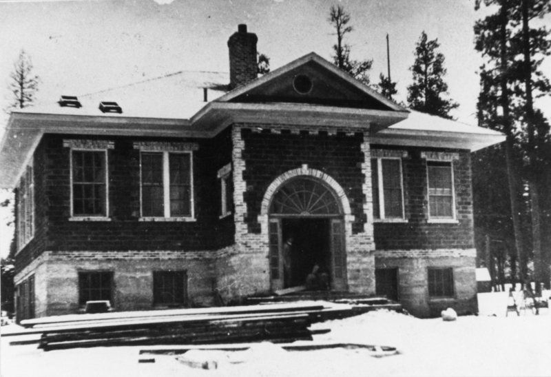A large, symmetrical brick building with a prominent arched entrance. The building has several tall windows and appears to be surrounded by snow and trees. A person or object is visible in the shadowed entranceway.