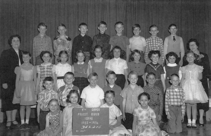 A group of children and two adults arranged in rows, dressed in a variety of outfits. The front row has children sitting with one holding a sign that reads "4th Grade Priest River Idaho 1955-1956." The children are smiling and standing on a stage with curtains in the background. Text reads: "4th GRADE PRIEST RIVER IDAHO 1955-1956 DB3-006 BY LEO'S".