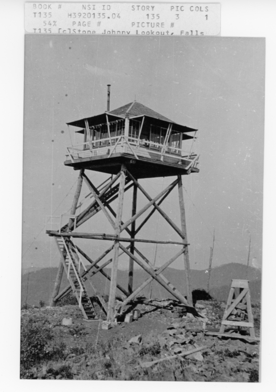 A tall wooden lookout tower with a small enclosed cabin at the top, elevated on a series of crisscrossed beams. The structure stands on a rocky landscape with mountainous terrain in the background. A ladder is attached to the side of the tower for access. Text reads: "The image has the following typed text near the top: - "BOOK #" - "NSI ID" - "STORY" - "PIC" - "COLS" - "T135" - "H3920135.04" - "135" - "3" - "1" - "54%" - "PAGE #" - "PICTURE #" - "T135 [c]Stone Johnny Lookout, Falls"