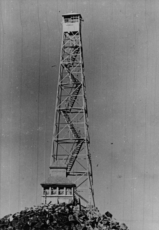 A tall lookout tower with a spiral staircase and a cabin at the top, situated on top of a rocky hill.