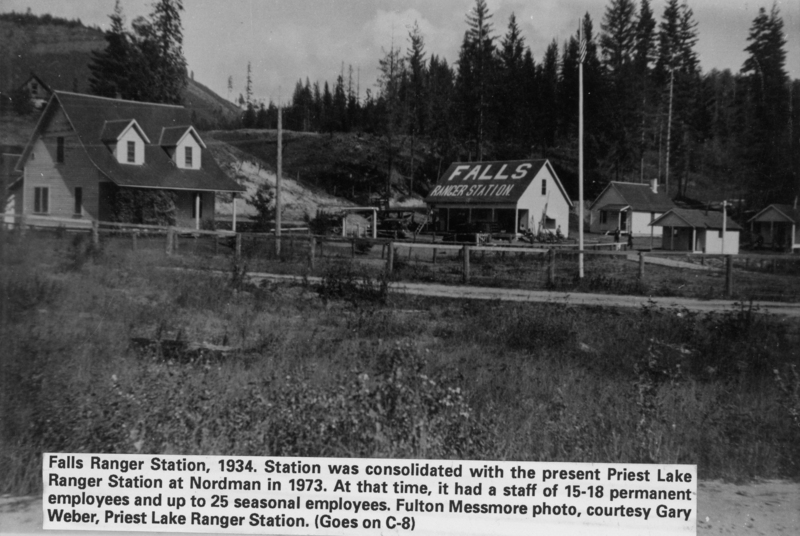A group of buildings labeled "Falls Ranger Station" is surrounded by a wooden fence and trees. There is a hillside in the background, and a large sign on the primary building reads "FALLS RANGER STATION." Additional smaller buildings are nearby. Text at the bottom provides historical context and information about staff. A label near the bottom reads: "Falls Ranger Station, 1934. Station was consolidated with the present Priest Lake Ranger Station at Nordman in 1973. At that time, it had a staff of 15-18 permanent employees and up to 25 seasonal employees. Fulton Messmore photo, courtesy Gary Weber, Priest Lake Ranger Station. (Goes on C-8)"