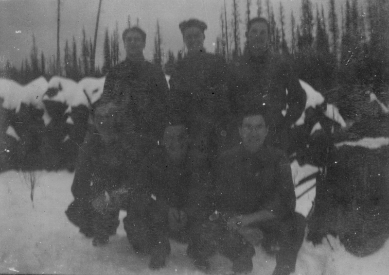 Six people standing and crouching in a snowy outdoor setting, with trees in the background.