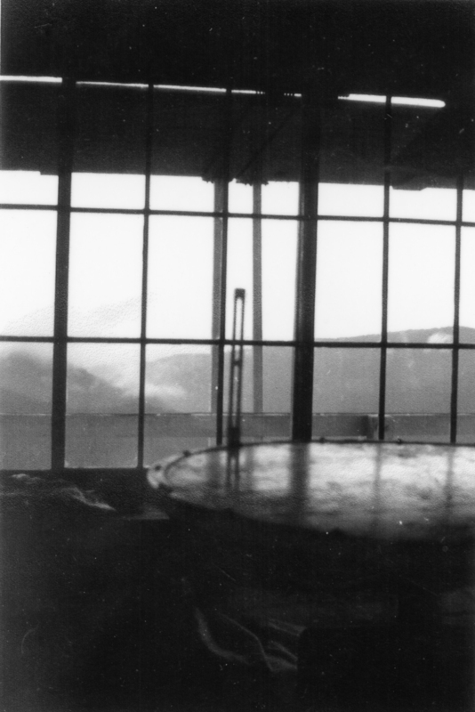 A round table near a large window with vertical and horizontal bars, with a view of mountains and clouds in the distance.