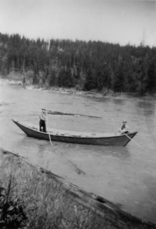Two people standing in a rowboat on a river, each holding a long pole. Riverbank with trees in the background.