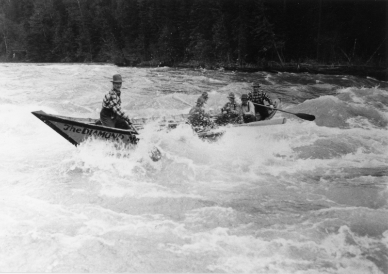 Several people are in a small boat navigating through rough waters. The water is choppy, and the boat is titled "The Diamond." The people appear focused on steering the boat. There are trees in the background.