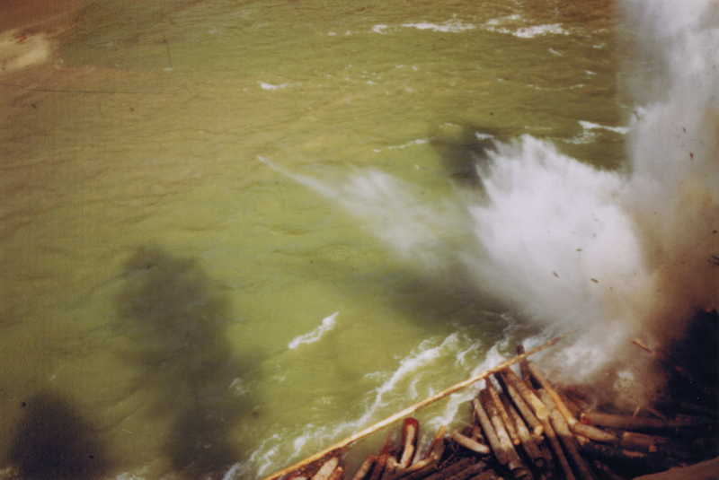 A large splash in a body of water with a group of logs floating at the bottom right.