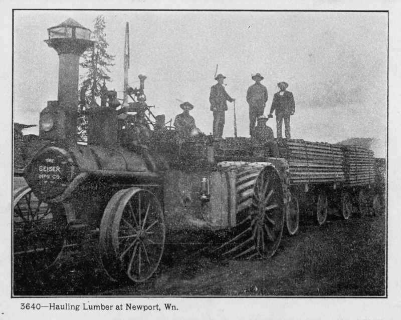 A large steam traction engine pulling a long trailer loaded with stacked lumber. Five men are standing on top of the lumber, wearing hats and work clothes. The scene takes place outdoors in a rural setting, with trees visible in the background. Text on the vehicle reads: "THE GEISER MFG. CO." Caption reads: "3640—Hauling Lumber at Newport, Wn. (Washington)."