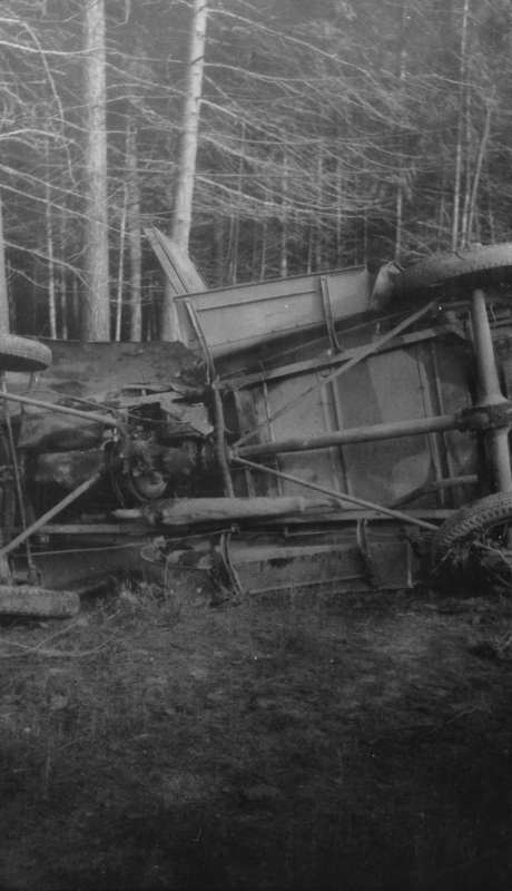 An overturned vehicle on its side with visible damage, surrounded by trees and grass.