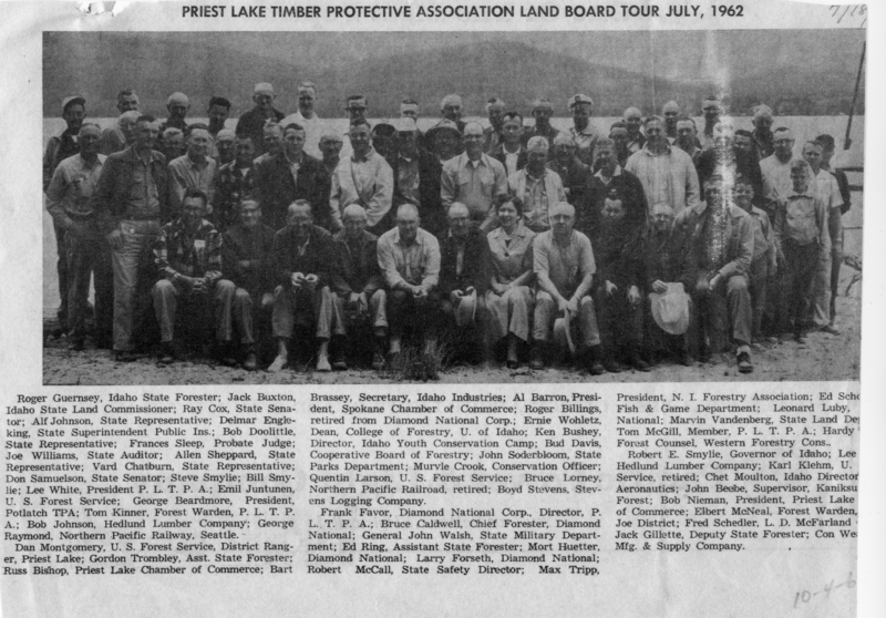 A large group of people is gathered together, posing for a picture. They are standing and sitting in rows, with some individuals seated in front. The group is outdoors, with a natural backdrop visible behind them. There are a mix of men and women, all dressed in similar attire, suggesting a formal or business setting. Typed text: Top Section: PRIEST LAKE TIMBER PROTECTIVE ASSOCIATION LAND BOARD TOUR JULY, 1962. Bottom Section (names and titles): Roger Guernsey, Idaho State Forester; Jack Buxton, Idaho State Land Commissioner; Ray Cox, State Senator; Alf Johnson, State Representative; Delmar Engleking, State Superintendent Public Ins.; Bob Doolittle, State Representative; Frances Sleep, Probate Judge; Joe Williams, State Auditor; Allen Sheppard, State Representative; Ward Chatburn, State Representative; Sam Sansevios, State Senator; Steve Smylie; Bill Smylie; Lee While, President P.L.T.P.A.; Emil Juntunen, U.S. Forest Service; George Beardmore, President, Kaniksu TPA; Tom Kinner, Forest Warden, P.L.T.P.A.; Bob Johnson, Hedlund Lumber Company; George Brassey, Secretary, Idaho Industries; Al Barron, President, Spokane Chamber of Commerce; Roger Billings, retired from Diamond National Corp.; Ernie Wohletz, Dean, College of Forestry, U. of Idaho; Ken Bushey, Director, Idaho Youth Conservation Camp; Bud Davis, Cooperative Board of Forestry; John Soderbloom, State Parks Department; Murvle Crook, Conservation Officer; Quentin Larson, U.S. Forest Service; Bruce Lomey, Northern Pacific Railroad, retired; Boyd Stevens, Stevens Logging Company; Dan Montgomery, U.S. Forest Service, District Ranger, Priest Lake; Gordon Trombley, Asst. State Forester; Russ Bishop, Priest Lake Chamber of Commerce; Bart Frank Favor, Diamond National Corp., Director, P.L.T.P.A.; Bruce Caldwell, Chief Forester, Diamond National; General John Walsh, State Military Department; Ed Ring, Assistant State Forester; Mort Huetter, Diamond National; Larry Forseth, Diamond National; Robert McCall, State Safety Director; Max Tripp, President, N.I. Forestry Association; Ed Schooler, Fish & Game Department; Leonard Luby, Diamond National; Marvin Vandenberg, State Land Department; Tom McGill, Member, P.L.T.P.A.; Hardy, Forest Counsel, Western Forestry Cons.; Robert E. Smylie, Governor of Idaho; Lee Hedlund Lumber Company; Karl Klehm, U.S. Forest Service, retired; Chet Moulton, Idaho Director Aeronautics; John Beebe, Supervisor, Kaniksu Forest; Bob Nieman, President, Priest Lake Chamber of Commerce; Elbert McNeal, Forest Warden, Joe District; Fred Schedler, L.D. McFarland; Jack Gillette, Deputy State Forester; Con Wead, Mfg. & Supply Company. Handwritten text: Near Top Right: 7/18, Bottom Right Corner: 104.