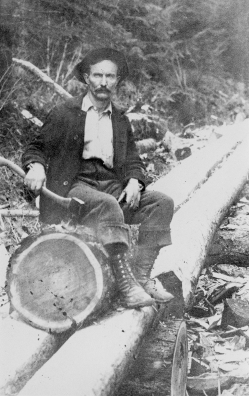 A man with a mustache sitting on a large tree log in a forested area, holding an axe in one hand and wearing a hat, coat, and boots.