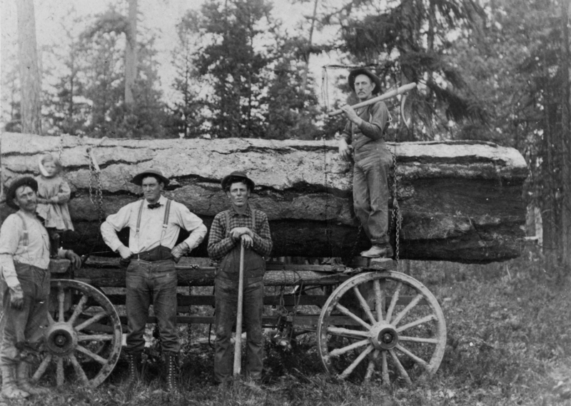 Four men and a child stand next to a large log on a wagon with big wooden wheels. One man is leaning on the log with a tool, and the child is sitting on the log. The background shows trees.
