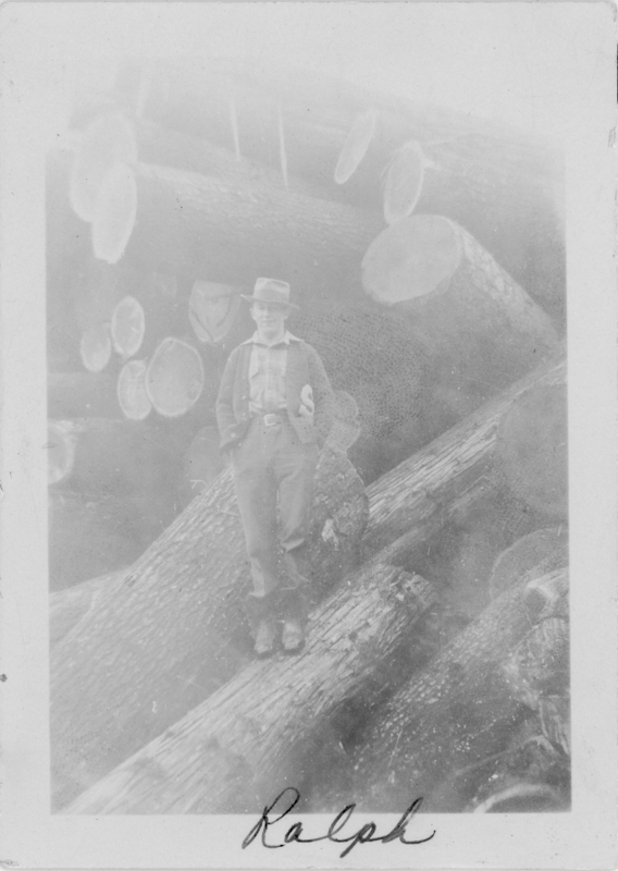 A man wearing a hat and casual attire is standing on a large pile of logs. His hands are in his pockets, and there are several cut tree trunks in the background. The name "Ralph" is written at the bottom.