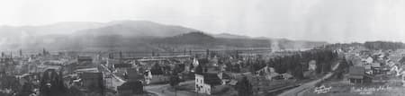 A black and white photograph of a town with mountains visible behind it. Text on the image reads, "Priest River Idaho Oct. 1921."