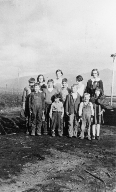 A group of children and a few adults standing together outdoors on a dirt ground, with a landscape visible in the background.