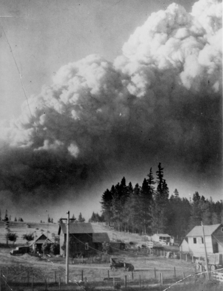 A rural scene with several houses surrounded by fields and trees. A large plume of smoke rises into the sky in the background. A car is parked near one of the houses, and a utility pole stands near the road.