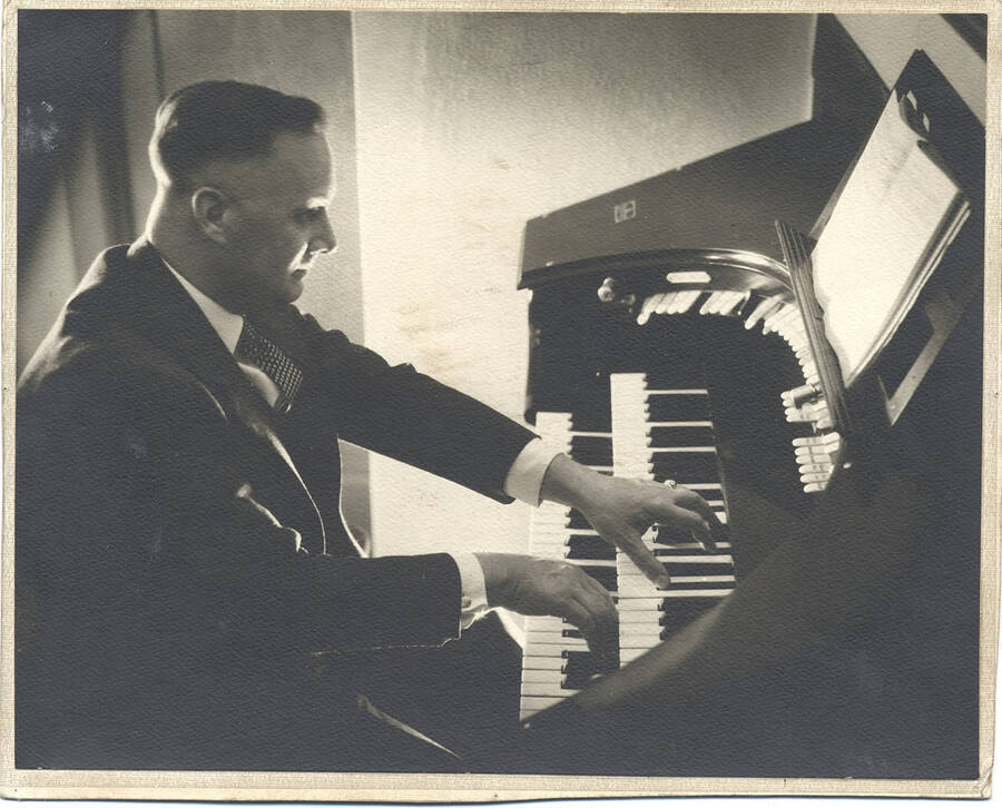 Photograph of Frank B. Robinson playing from a book of sheet music on his pipe organ.