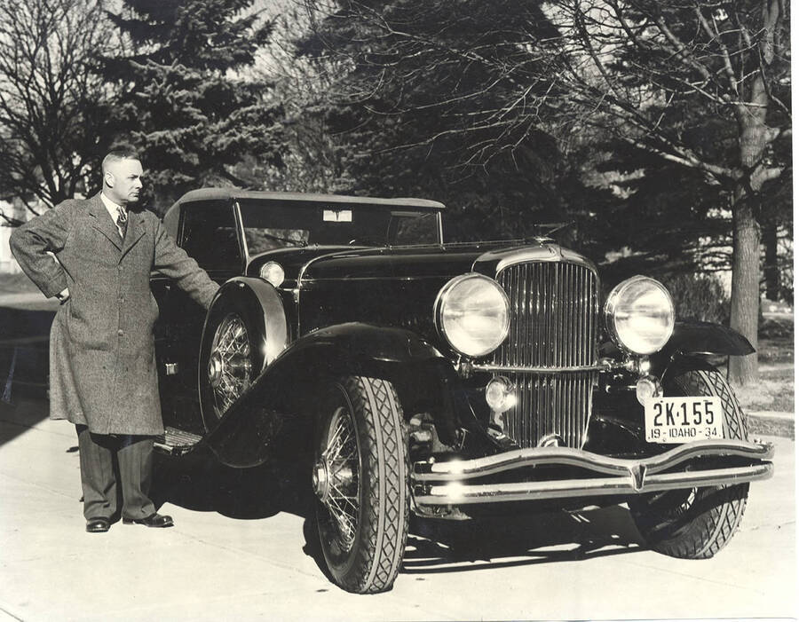 Photograph of Frank B. Robinson standing outside the passenger side of his Duesenberg Convertible Coupe with a park in the background.