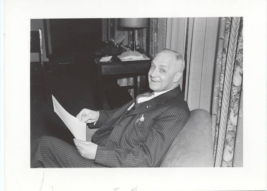 Photograph of older Frank B. Robinson in pin-striped suit sitting in a chair holding paper.