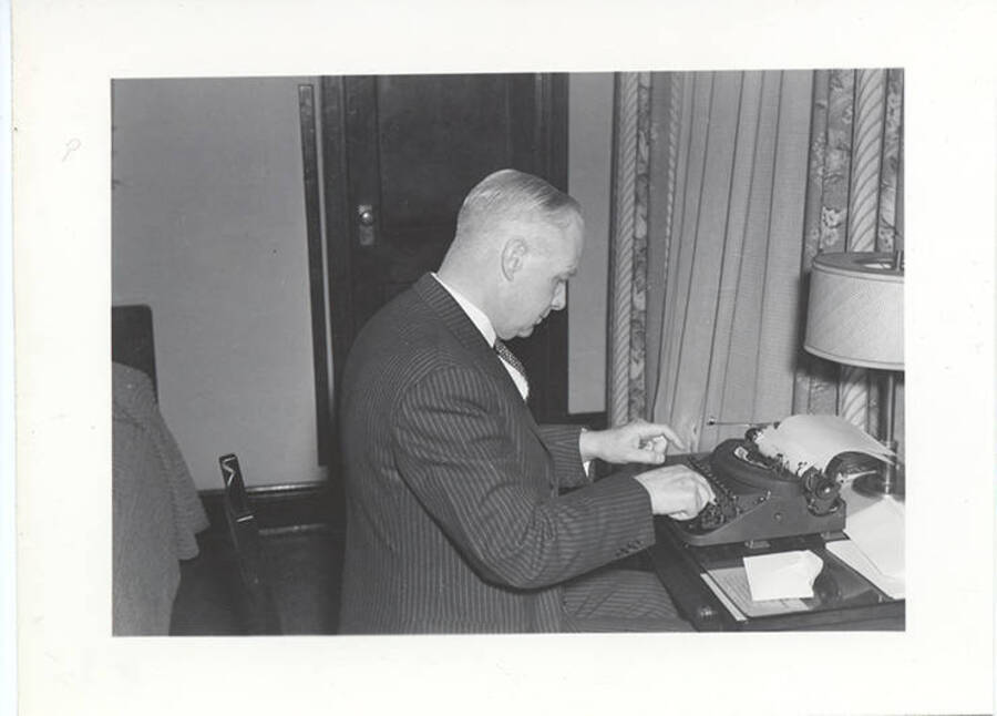 Photograph of Frank B. Robinson in a pin striped suit sitting at a loaded typewriter typing a document.