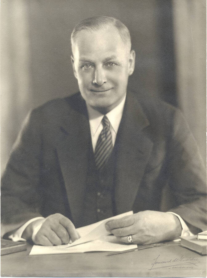 Portrait of middle-aged Frank B. Robinson in three piece suit sitting at a desk with paper and pen beneath his hands.