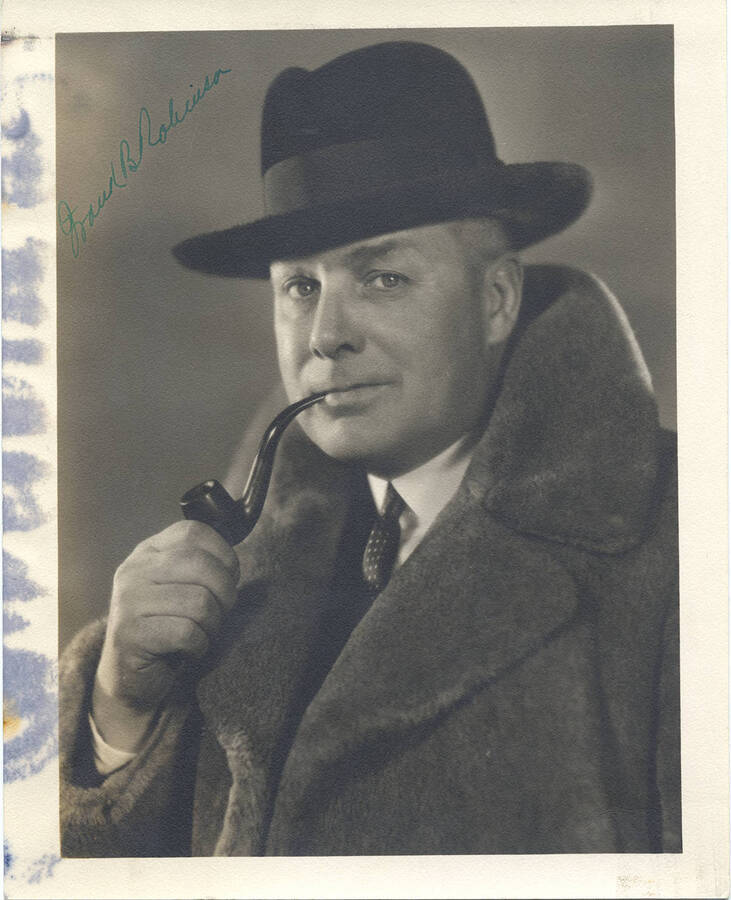 Signed portrait of middle-aged Frank B. Robinson holding a pipe and dressed in a three piece suit, large fur coat, and homburg hat.