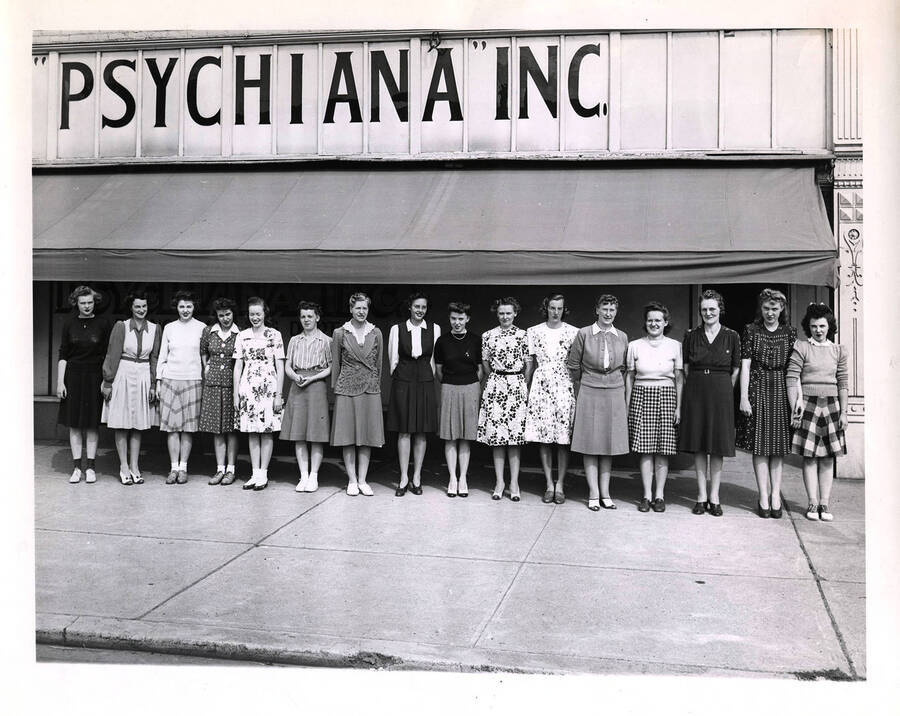 Photograph of all women staff from Psychiana clerical and bookkeeping standing in front of the Branch Mailing Department at 1st and Main Street in Moscow, Idaho. This building is two stories and occupies half a block.