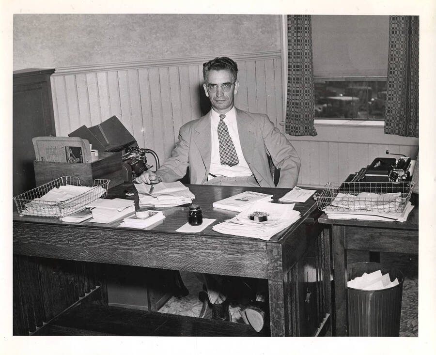 Photograph of W.W. DeBolt sitting at his desk beside a Dictaphone and typewriter with several stacks of paper and a hardback book with Frank B. Robinson's face on the cover. [Later illustrations of this man on Psychiana documents may indicate this is actually C.W. Tenney, and was mislabeled.]