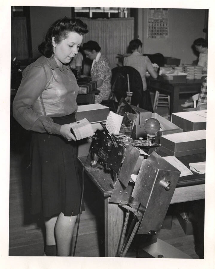 Photograph depicts a female Psychiana staff member loading handfuls of envelopes into a sorter machine in preparation for mailing.