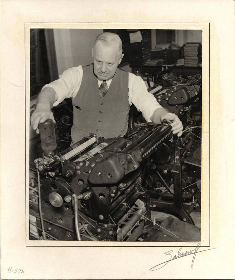 Photograph depicts Frank. B. Robinson with his sleeves rolled up, loading a small printing press with ink from a black container.