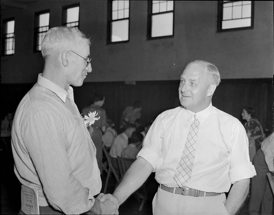 Photograph depicts Frank B. Robinson shaking hands with Carl Grief, President of the Uniontown Stock Show, in a large dining room/gymnasium.