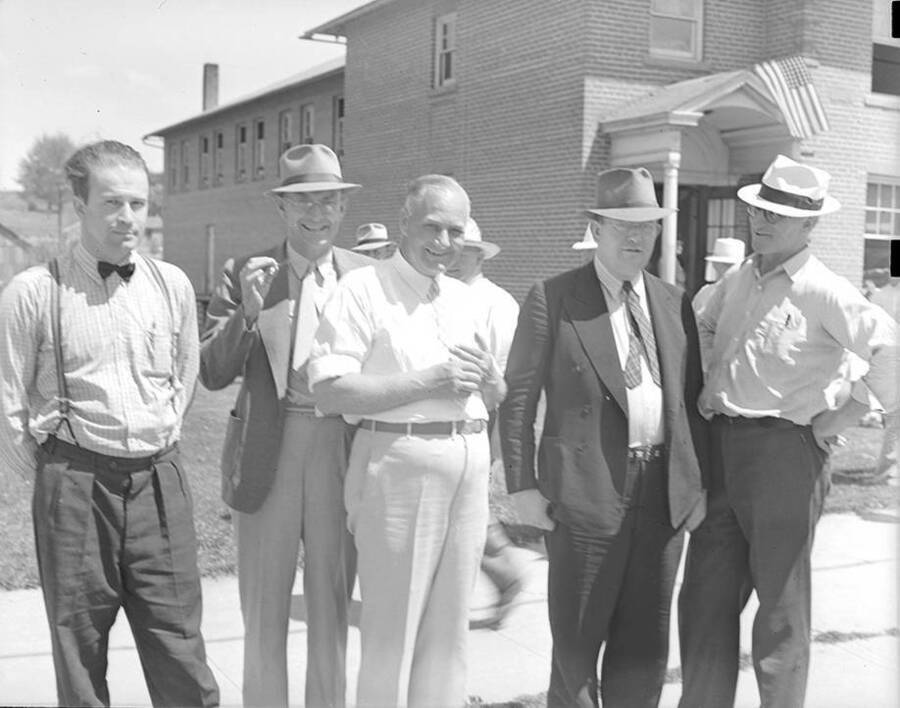 Photograph depicts Frank B. Robinson smiling and standing in front of a large brick Uniontown building along with four unidentified men.