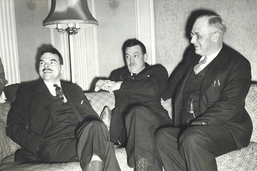 Photograph depicts Frank B. Robinson (right) sitting on a couch with politician Thomas E. Dewey (left) and an unidentified pressman, all in formal attire.