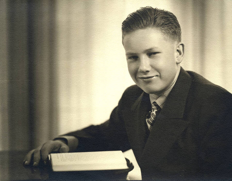 Portrait depicts Alfred B. Robinson, child, in a suit and tie sitting at a desk and leaning over a book.