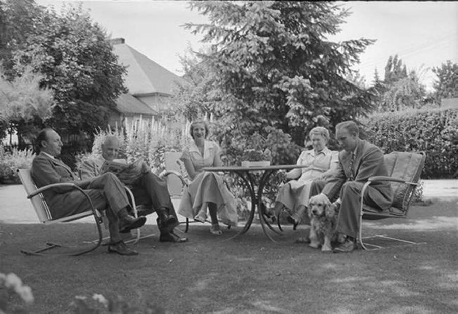 Photograph depicts Robinson family, in Frank B. Robinson and Pearl Bey Robinson's older years, sitting outside on law furniture around a table with a cocker spaniel.